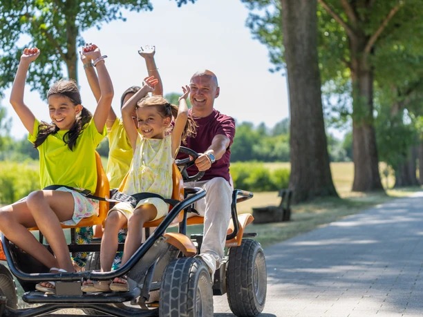 Gocart ausleihen im Monheimer Landschaftspark Familien genießen eine fröhliche Fahrt mit einem großen Gokart auf einem sonnigen Parkweg.