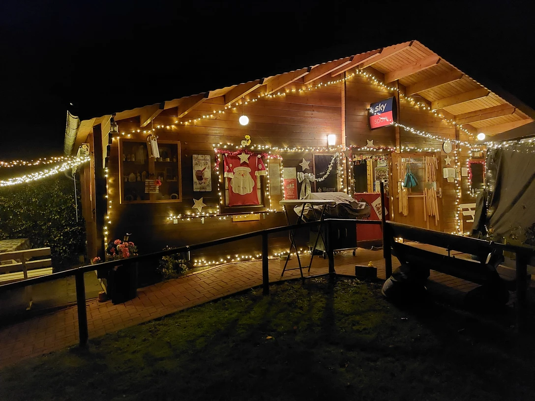 Glühhütte Eine Holzalmhütte erstrahlt nachts mit bunten Lichterketten, warme Atmosphäre durch Dekoration.