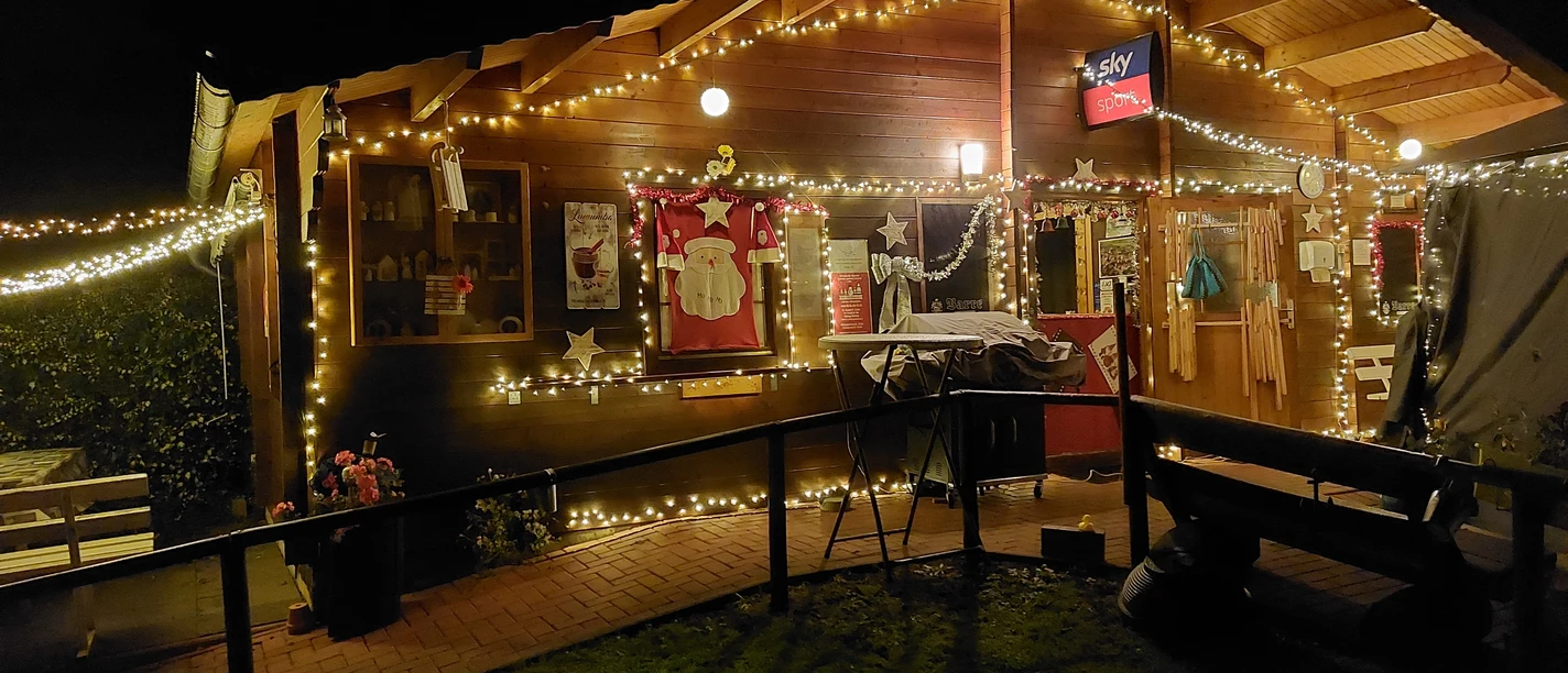 Eine Holzalmhütte erstrahlt nachts mit bunten Lichterketten, warme Atmosphäre durch Dekoration.