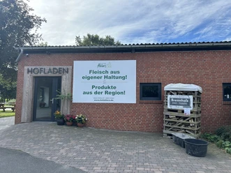 Hofladen Hof Ahlers Dörpen ©Emsland Tourismus GmbH (1).JPEG Backsteinbau mit Eingang zum Hofladen, Pflanzkübeln und Brennholzstapel vor dem Gebäude
