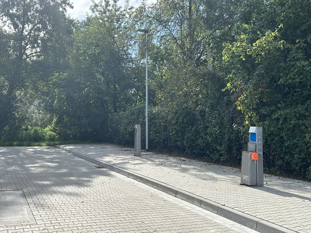 Wohnmobilstellplatz Schützenplatz Dörpen ©Emsland Tourismus GmbH (3).JPEG Gepflasterter Wohnmobilstellplatz mit Versorgungssäule, umgeben von Bäumen und dichter Vegetation.