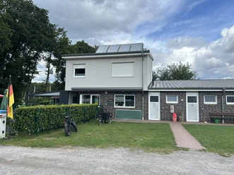 Modernes Sanitärgebäude mit Kiosk auf dem Campingplatz, davor Rasenfläche und geparkte Fahrräder.