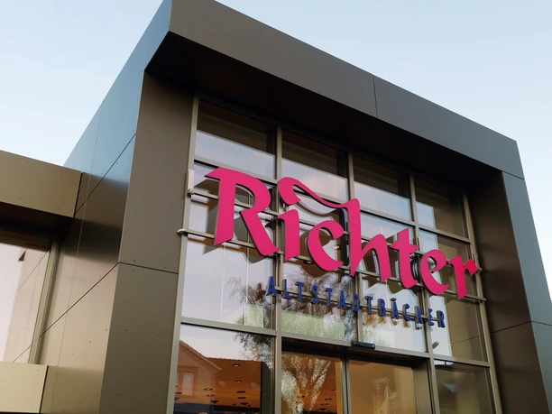 Close-up of an angular façade with large glass surfaces. Pink inscription: "Richter" underneath in blue: "Altstadtbäcker"
