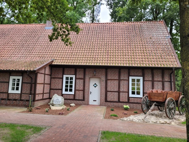 Heimathaus Lahn ©Emsland Tourismus GmbH.jpg Fachwerkhaus mit roten Dachziegeln, weißer Eingangstür, Steinplatte und Holzkarre im Vorgarten.