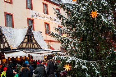 Man sieht ein Banner an der Hauswand vom Schloss Trebsen auf dem Advent im Schloss steht. im Vordergrund ist ein weihnachtlicher Stand und ein Weihnachtsbaum.