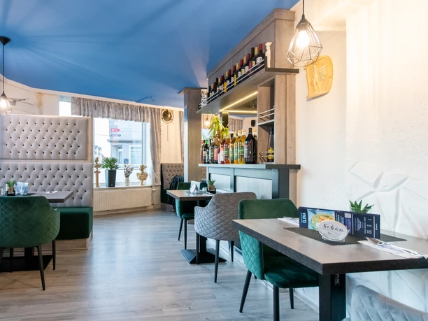 Modern dining room in blue, green and gray. Comfortable chairs at the tables in front of large windows and a bar