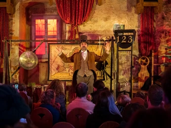 Schloss Trebsen weihnachtliche Theateraufführung Zusehen ist ein Schauspiler der als Entdecker verkleidet ist, vor einem Publikum. Auf der Bühe stehen Requisiten.You can see an actor dressed as an explorer in front of an audience. There are props on the stage.Před publikem můžete vidět herce převlečeného za průzkumníka. Na jevišti jsou rekvizity.Przed publicznością widać aktora przebranego za odkrywcę. Na scenie znajdują się rekwizyty.Je ziet een acteur verkleed als ontdekkingsreiziger voor een publiek. Er staan rekwisieten op het podium.Si vede un attore vestito da esploratore davanti a un pubblico. Sul palco ci sono oggetti di scena.