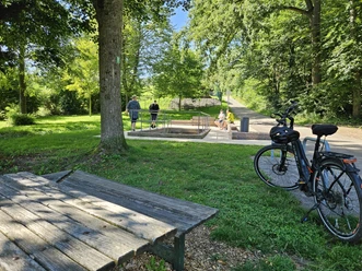 Bad Driburg_Wasser-Tretbecken Alhausen Ein Wasserkneippbecken in Alhausen umgeben von Bäumen und Spaziergängern, im Vordergrund ein Fahrrad.