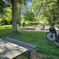 Bad Driburg_Wasser-Tretbecken Alhausen Ein Wasserkneippbecken in Alhausen umgeben von Bäumen und Spaziergängern, im Vordergrund ein Fahrrad.