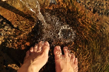 Füße in klarem, flachem Wasser, leicht bewegt von einem sanft fließenden Wasserstrahl.