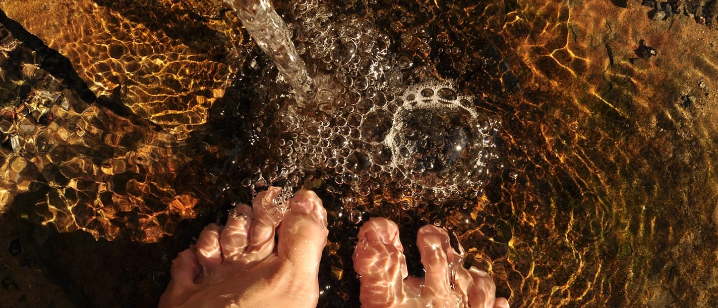 Füße in klarem, flachem Wasser, leicht bewegt von einem sanft fließenden Wasserstrahl.