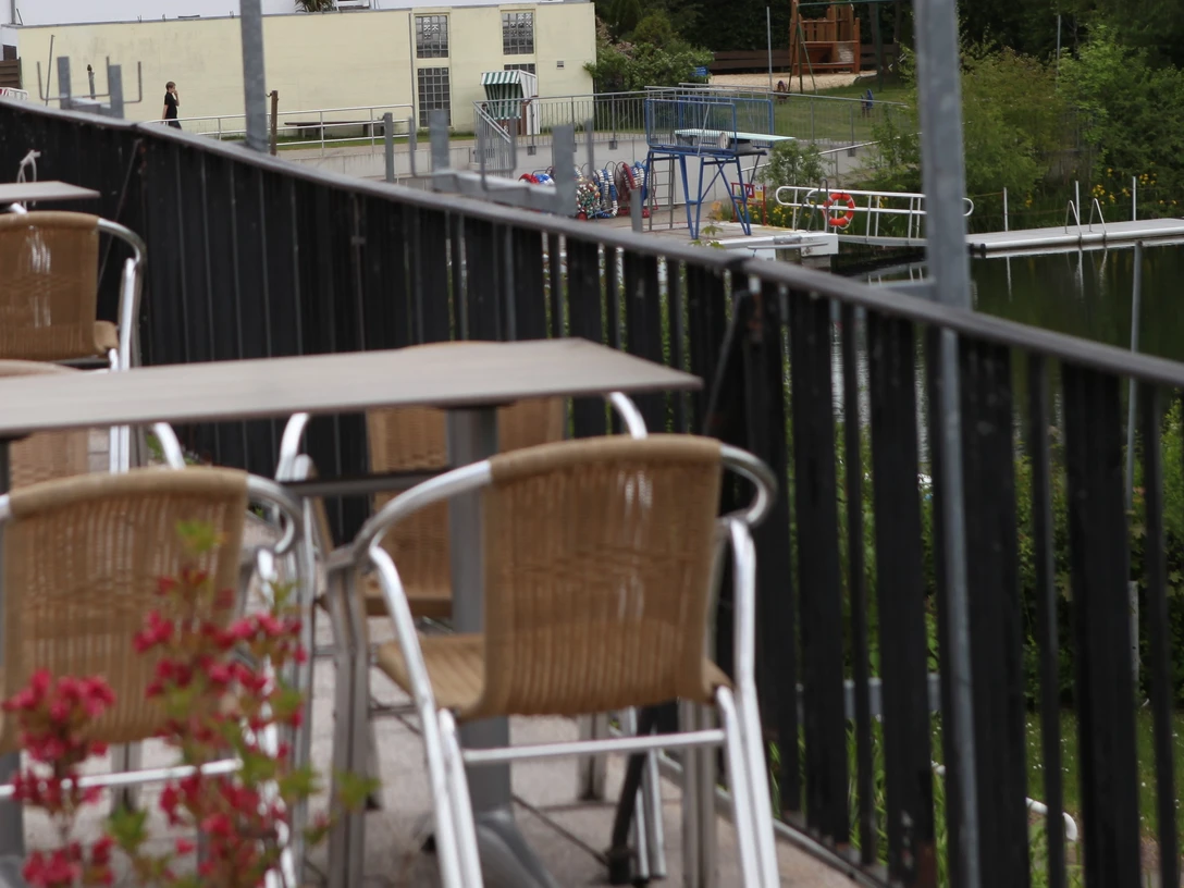 Tische und Stühle auf einer Terrasse, im Hintergrund ein See