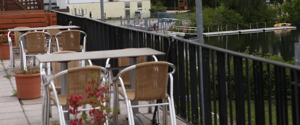 Fümmelsee Terrasen.JPG Tische und Stühle auf einer Terrasse, im Hintergrund ein See