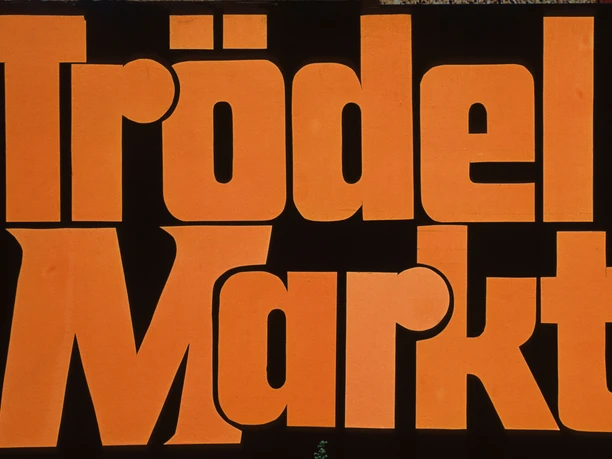 Trödelmarkt Rahden Große, orangefarbene Schrift auf schwarzem Hintergrund mit dem Text "Trödel Markt".
