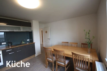 pension_luci_küche1a.jpg Helle Küche mit Esstisch und sechs Stühlen, moderne Ausstattung mit dunklen Schränken und Pflanze.