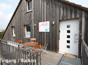 pension_luci_eingang_balkon1a.jpg Eingang der Pension Luci mit Holzbalkon und Sitzgruppe, modern gestaltet, vor einer Holzfassade.