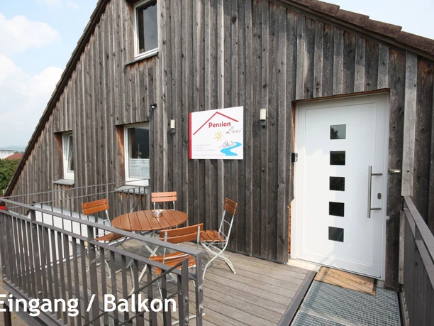 pension_luci_eingang_balkon1a.jpg Eingang der Pension Luci mit Holzbalkon und Sitzgruppe, modern gestaltet, vor einer Holzfassade.