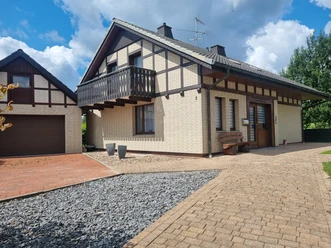 Ferienhaus Eggetal Fachwerk-Ferienhaus mit Balkon, Ziegeldach und gepflastertem Eingang, daneben ein Carport.