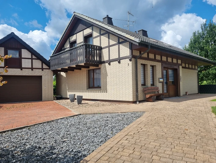 Ferienhaus Eggetal Fachwerk-Ferienhaus mit Balkon, Ziegeldach und gepflastertem Eingang, daneben ein Carport.