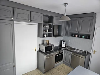 Ferienhaus Eggetal_Küche Moderne Küche mit grauen Schränken, integrierten Geräten, offener Regalablage und heller Keramikfliese.