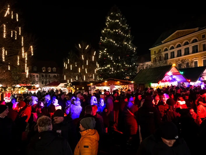 Delitzscher Adventsmarkt Marktplatz Zusehen ist eine Menschengruppe am Abend auf dem Delitzscher Marktplatz. Im Hintergrund sind beleuchtete Nadelbäume und weihnachliche Stände.