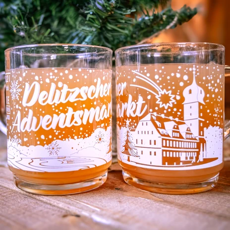 Vidíte dvě sklenice Pusch s potiskem "Delitzscher Adventsmarkt". Sklenice obsahují tekutinu podobnou tekutině Pusch.