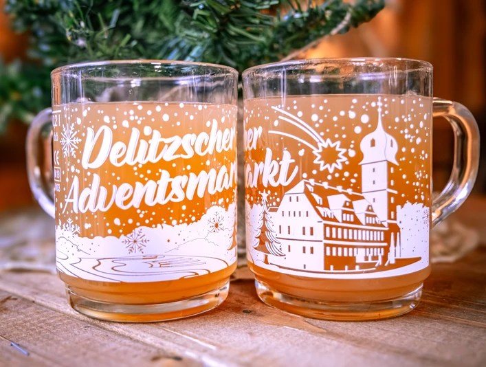 Delitzscher Adventsmarkt Punschglas Zusehen sind zwei Puschgläser mit dem Aufdruck "Delitzscher Adventsmarkt". Im Glas ist eine Puschähnliche Flüssigkeit.