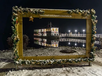 weisse-flotte-im-bilderrahmen-weihnachtlich.jpg Weihnachtlich geschmückter Bilderrahmen mit beleuchtetem Ausflugsschiff der Weissen Flotte an verschneitem Steg bei Nacht.