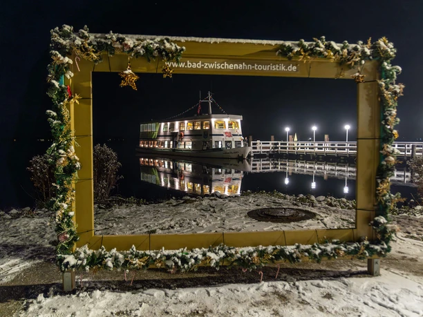 weisse-flotte-im-bilderrahmen-weihnachtlich.jpg Weihnachtlich geschmückter Bilderrahmen mit beleuchtetem Ausflugsschiff der Weissen Flotte an verschneitem Steg bei Nacht.
