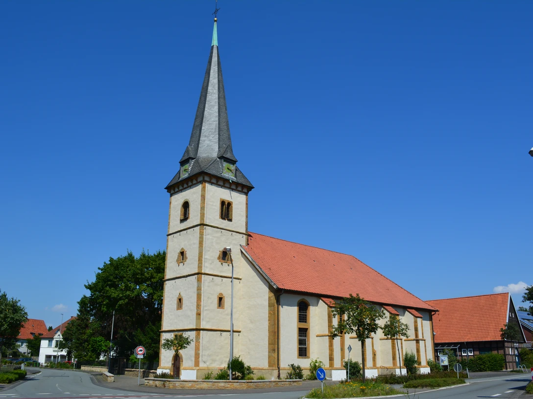 Brockhagen - St. Georgskirche Evangelische Kirche mit spitzem Turm und roten Dachziegeln vor blauem Himmel in ländlicher Umgebung.
