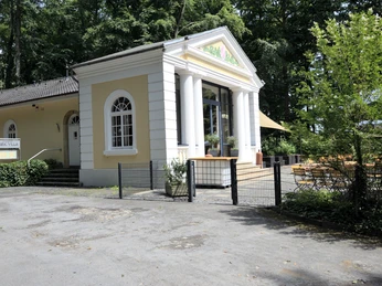 Ein charmantes Gebäude im klassizistischen Stil mit weißen Säulen, vor einem grünen Wald gelegen.