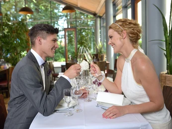 Elegantes Paar beim Anstoßen mit Sekt an einem Tisch in einem stilvollen Restaurantambiente.