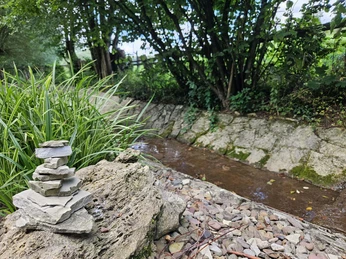 Fluss fließt durch Pömbsen, daneben ist ein gestapelter Turm aus Steinen.