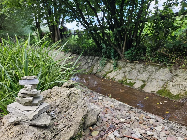 Bad Driburg_Wasser-Tretbecken Poembsen Fluss fließt durch Pömbsen, daneben ist ein gestapelter Turm aus Steinen.