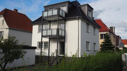 P1010027.JPG Ein dreistöckiges, modernes Wohnhaus mit Balkonen und weißen Wänden neben Häusern unter blauem Himmel.