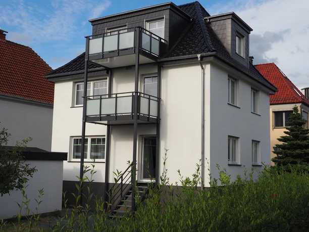 P1010027.JPG Ein dreistöckiges, modernes Wohnhaus mit Balkonen und weißen Wänden neben Häusern unter blauem Himmel.