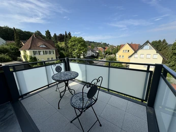 IMG_6447.jpg Zwei schmiedeeiserne Stühle und ein Tisch auf einem Balkon mit Blick auf ein Wohngebiet und Hügel.