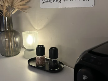 IMG_0943.jpeg Wand mit Schriftzug "Schön, dass du da bist!", neben einer Tischlampe und Gewürzmühlen auf einem Tablett.