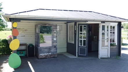 Regiomat Hof Lüssing ©Emsland Tourismus GmbH Kleines Hofgebäude mit Verkaufsautomat für regionale Produkte und Eingangstür im Sonnenlicht.