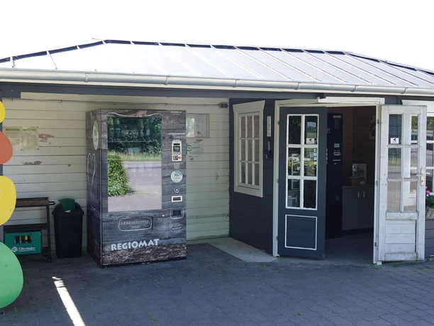 Regiomat Hof Lüssing ©Emsland Tourismus GmbH Kleines Hofgebäude mit Verkaufsautomat für regionale Produkte und Eingangstür im Sonnenlicht.