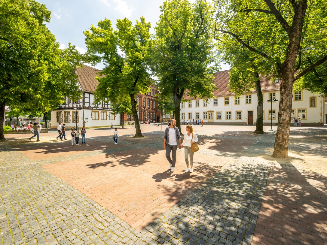 Historischer Platz mit Kopfsteinpflaster, umgeben von alten Fachwerkhäusern und grünen Bäumen.