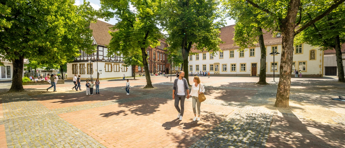 Historischer Platz mit Kopfsteinpflaster, umgeben von alten Fachwerkhäusern und grünen Bäumen.