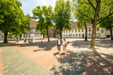 Bielefeld-Klosterplatz-Teutoburger-Wald-Bielefeld Marketing-D.Ketz Historischer Platz mit Kopfsteinpflaster, umgeben von alten Fachwerkhäusern und grünen Bäumen.