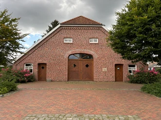 Heimathaus Bockhorst ©Emsland Tourismus GmbH (1).JPEG Backsteinbau mit roten Dachziegeln und hölzernen Türen, umgeben von blühenden Büschen und Bäumen.