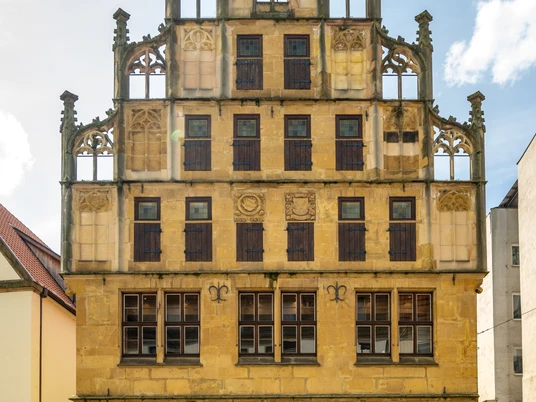 Bielefeld-Crüwell-Teutoburger-Wald-D-Ketz-124.jpg Historisches Gebäude mit reich verzierter Fassade, gelbem Stein und zahlreichen Fenstern. Vorne verläuft eine Straße.