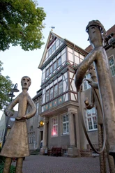 Fachwerkhaus mit reich verziertem Giebel im Hintergrund, Skulpturen einer Familie im Vordergrund.