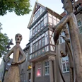 Fachwerkhaus mit reich verziertem Giebel im Hintergrund, Skulpturen einer Familie im Vordergrund.
