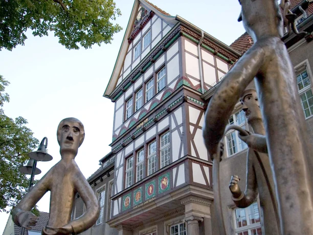 Stadt Petershagen_Petershagen_Evelyn Hotze_Altes Amtsgericht_Giebel_Skulpturenfamilie im Vordergrund_hoch.jpg Fachwerkhaus mit reich verziertem Giebel im Hintergrund, Skulpturen einer Familie im Vordergrund.