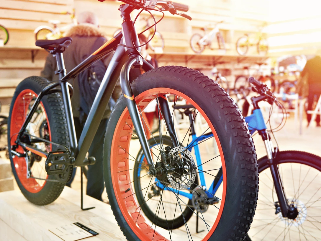 2 Rad Marcus Berger.png Im Vordergrund steht ein schwarzes Mountainbike, das für unebenes Gelände optimiert ist. Im Hintergrund sind weitere Fahrräder zu sehen, die ebenfalls für den Outdoor-Einsatz geeignet sind.