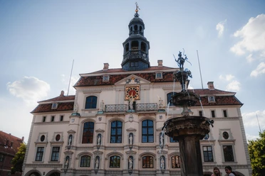 Rathaus Lüneburg Rathaus Lüneburg mit heller Fassade, Statuen, Uhr und dem Lunabrunnen im Vordergrund.